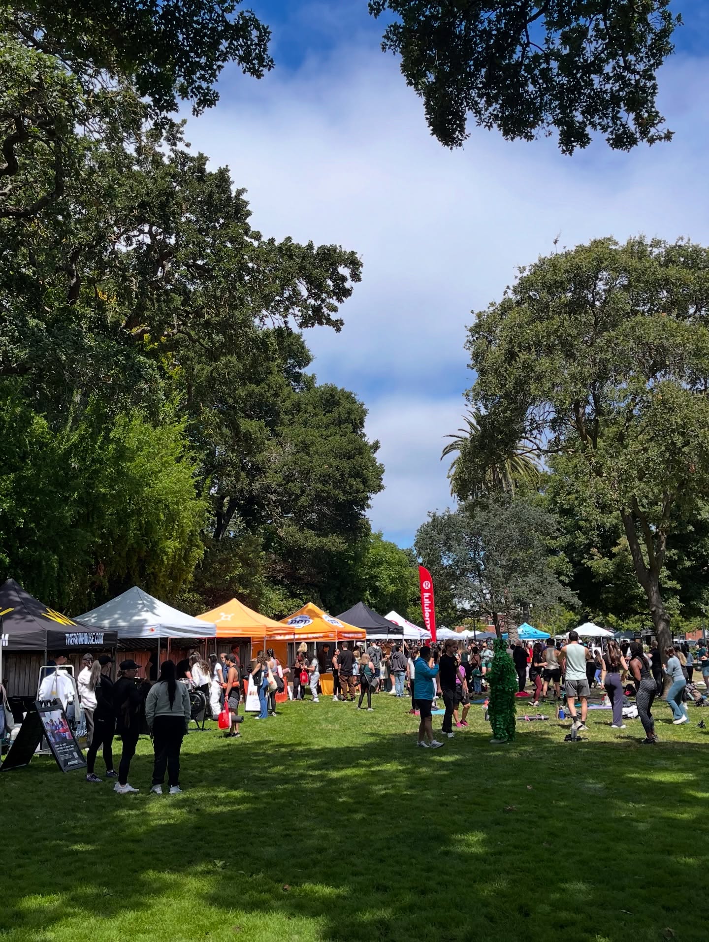 People gathering among booths and trees at Fit Fest
